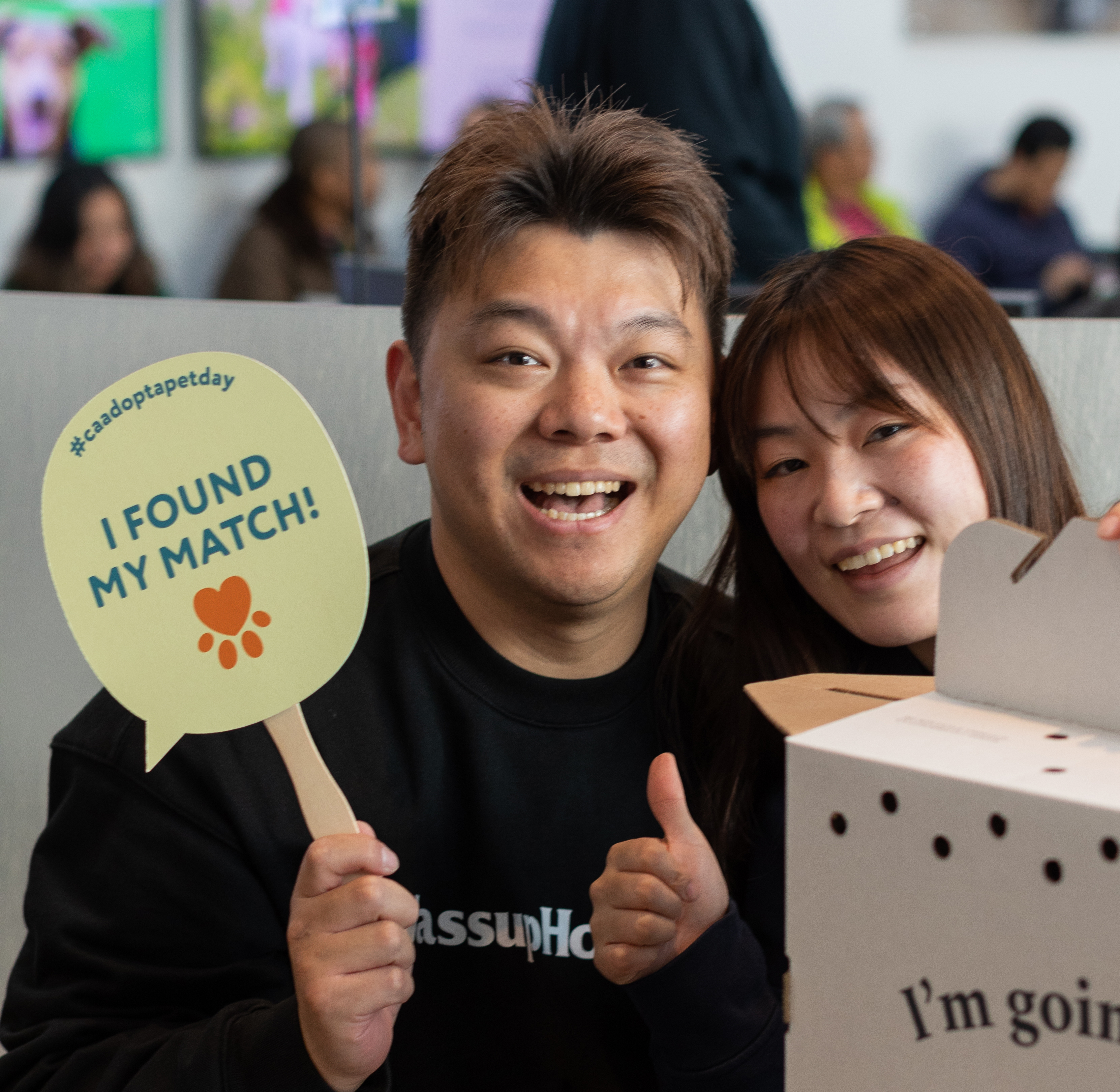 Two smiling people posing together indoors, one holding a sign that says ‘I found my match!’ and the other holding a cardboard box